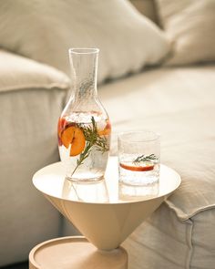 a glass vase with oranges and water on a table in front of a couch