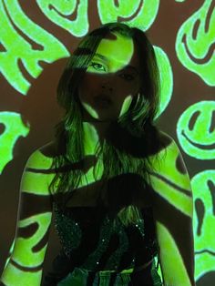 a woman standing in front of a wall with green and black designs projected on it