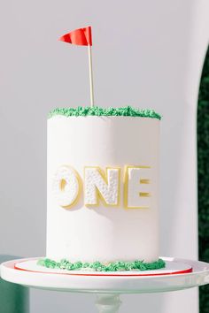 a white cake with green frosting and a red flag on top that says one