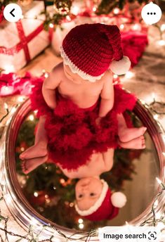 a baby wearing a santa hat sitting on top of a mirror next to christmas decorations