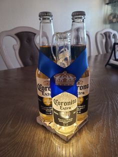 two bottles of corona extra are sitting on a wooden table with chairs in the background