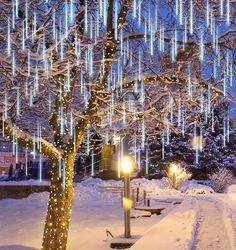 a tree with blue lights hanging from it's branches in the middle of a snow covered park