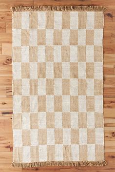 a tan and white checkered rug with fringes on top of wood flooring