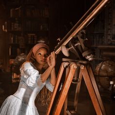 a woman in a white dress is looking through a telescope at an antique type machine