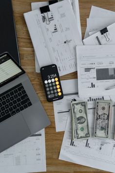 an open laptop computer sitting on top of a wooden desk covered in papers and money