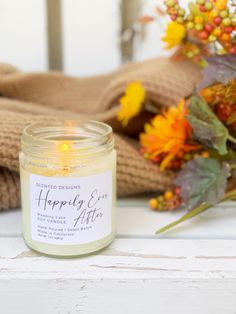 a candle sitting on top of a white table next to some flowers and sweaters