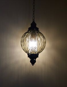 a glass light hanging from a chain in a room with white walls and shadows on the wall