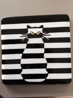 a black and white cat with yellow eyes sitting on top of a striped square plate