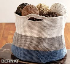 a crocheted basket with yarn balls in it on a wooden table next to a wall