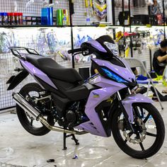 a purple motorcycle parked inside of a building next to other motorcycles and people working on it