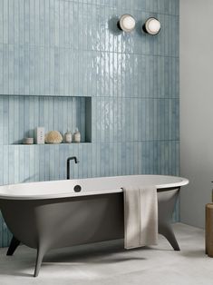 a bath tub sitting next to a wall with blue tiles on it and a towel hanging from the side