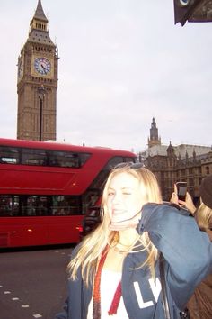 a woman standing in front of a red double decker bus on a city street with big ben in the background