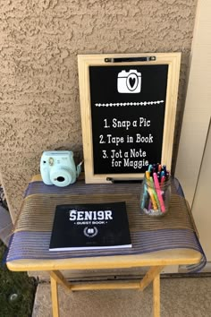 a small table with a sign on it and some pens, pencils, and a camera