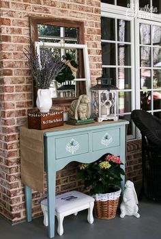 a blue table with flowers on it and a mirror in the window behind it that is next to a white teddy bear