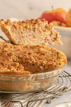 a piece of pie is being lifted out of the pie dish by a fork with an apple in the background