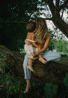 two women hugging each other while sitting on a tree branch