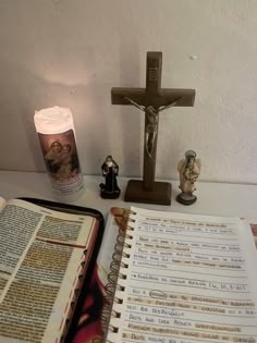 an open bible next to a lit candle and figurines on a table with a cross