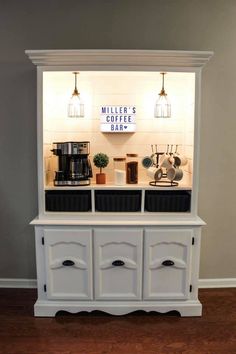 a white cabinet with two black sinks and some lights on the wall above it in a living room