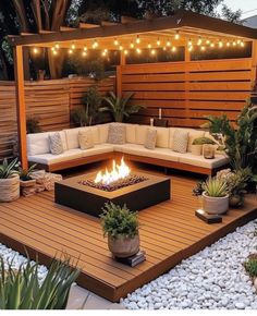 an outdoor fire pit surrounded by plants and rocks with lights strung over the back wall