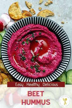 beet hummus in a bowl surrounded by crackers and vegetables