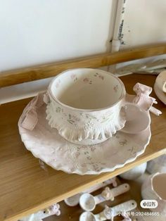 a white cup and saucer sitting on top of a wooden shelf next to other dishes