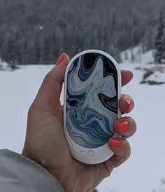 a woman holding up her cell phone in front of the snow covered mountains and trees