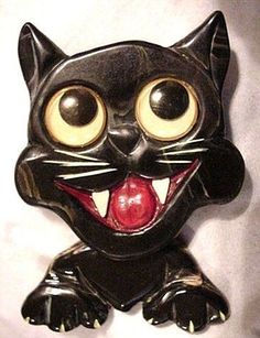 a ceramic black cat with big eyes and mouth wide open, sitting on a white surface