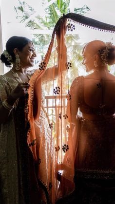 two women standing next to each other in front of a window with an orange curtain