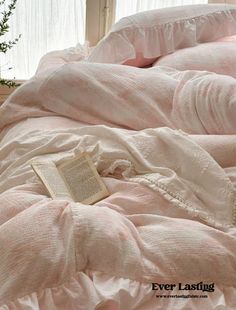 an open book laying on top of a pink comforter next to a white window