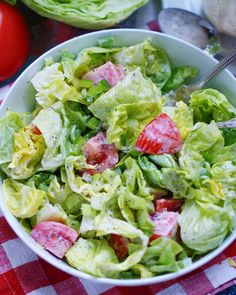 a salad with lettuce and tomatoes in a bowl on a checkered table cloth