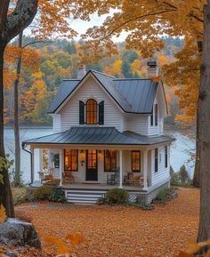 a white house surrounded by trees with fall leaves on the ground and water in the background