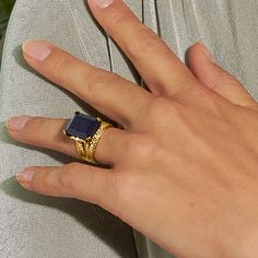 a woman's hand wearing a gold ring with a blue stone in the middle