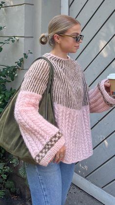 a woman is holding a cup and looking at her cell phone while standing in front of a house