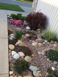 a garden with rocks and flowers next to a house on the side of the road