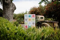 an old truck with a quilt on the back parked next to a tree and shrubbery