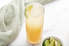 a glass of lemonade with limes on the side and a bowl of sliced limes next to it