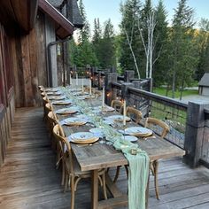 an outdoor dining table set with place settings on a deck overlooking a wooded area in the woods