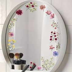 a mirror with flowers painted on it and makeup brushes in front of the mirror's reflection