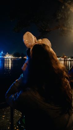 a woman sitting on a bench next to the water at night with balloons floating in the air