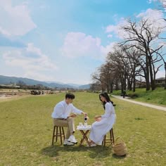 two people sitting at a picnic table in the middle of a grassy field with trees