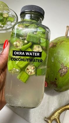 a person holding a jar filled with water next to two green apples and coconuts