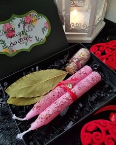 two pink candles in a black box on a table next to some decorative items and a lit candle