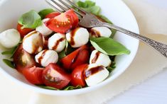 a white bowl filled with mozzarella and cherry tomatoes on top of green leaves