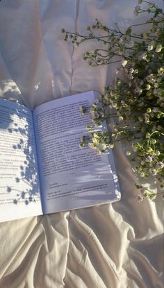 an open book sitting on top of a bed next to flowers