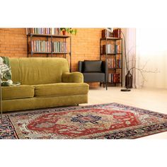 a green couch sitting on top of a rug in front of a book shelf filled with books