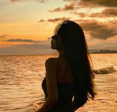 a woman standing in the water at sunset with her hair blowing back and eyes closed