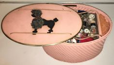 a pink hat box with a poodle on it and sewing needles in the bottom