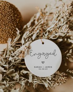 an engaged ornament hanging from a tree branch in front of some dried flowers