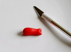 a red object sitting next to a pen on top of a white table with a silver tip