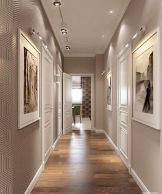 a long hallway with pictures on the wall and wood flooring, along with white framed artwork